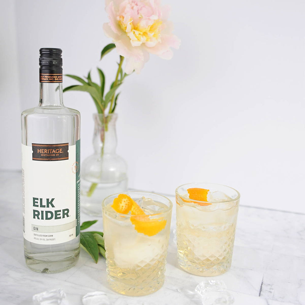 A bottle of HDC Elk Rider Gin is displayed next to two full glasses of the Negroni D'Or. 