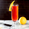 A cocktail that features HDC Blood Orange Vodka and Rose Prosecco with a thick orange peel to garnish.