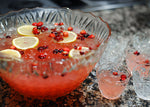 A crystal punch bowl full of a red vodka and bourbon based cocktail (using HDC Raspberry Vodka and BSB - Brown Sugar Bourbon). There are floating lemon wheels and fresh cranberries in the glasses of punch as well.