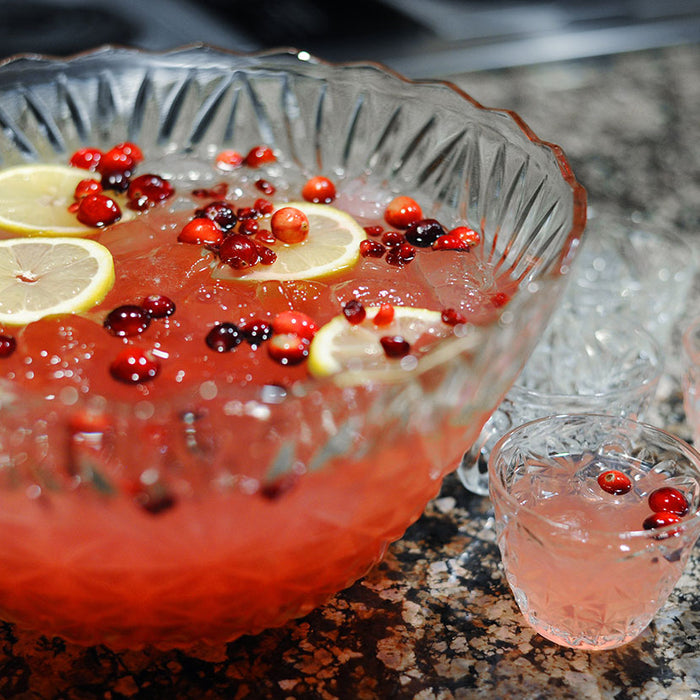 A crystal punch bowl full of a red vodka and bourbon based cocktail (using HDC Raspberry Vodka and BSB - Brown Sugar Bourbon). There are floating lemon wheels and fresh cranberries in the glasses of punch as well.