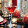 A beautiful table setting with crystal vases and candles. A HDC Pomegranate vodka-based cocktail drink in a stemmed martini glass.