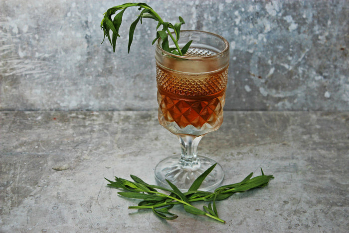 A goblet of Smoky Elk Rider Cocktail featuring both HDC Elk Rider Bourbon and HDC Elk Rider Blended Whiskey topped with fresh tarragon leaves.
