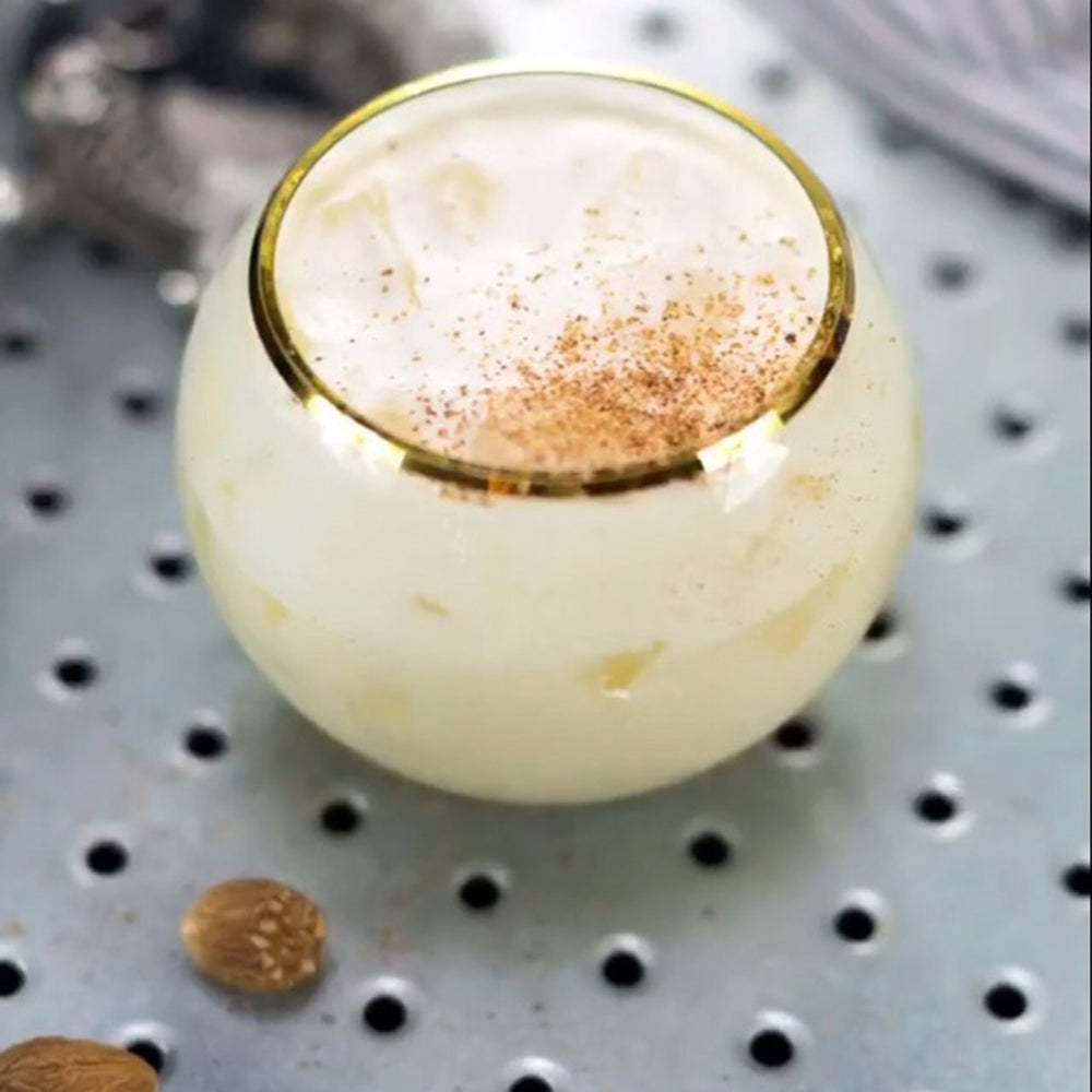 A gold-rimmed glass full of the Vanilla Vodka Tuaca Cream cocktail with grated nutmeg on top.