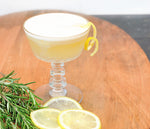 A cocktail goblet with the Rosemary Maple Whiskey Sour featuring HDC Elk Rider Bourbon and garnished with a lemon twist.