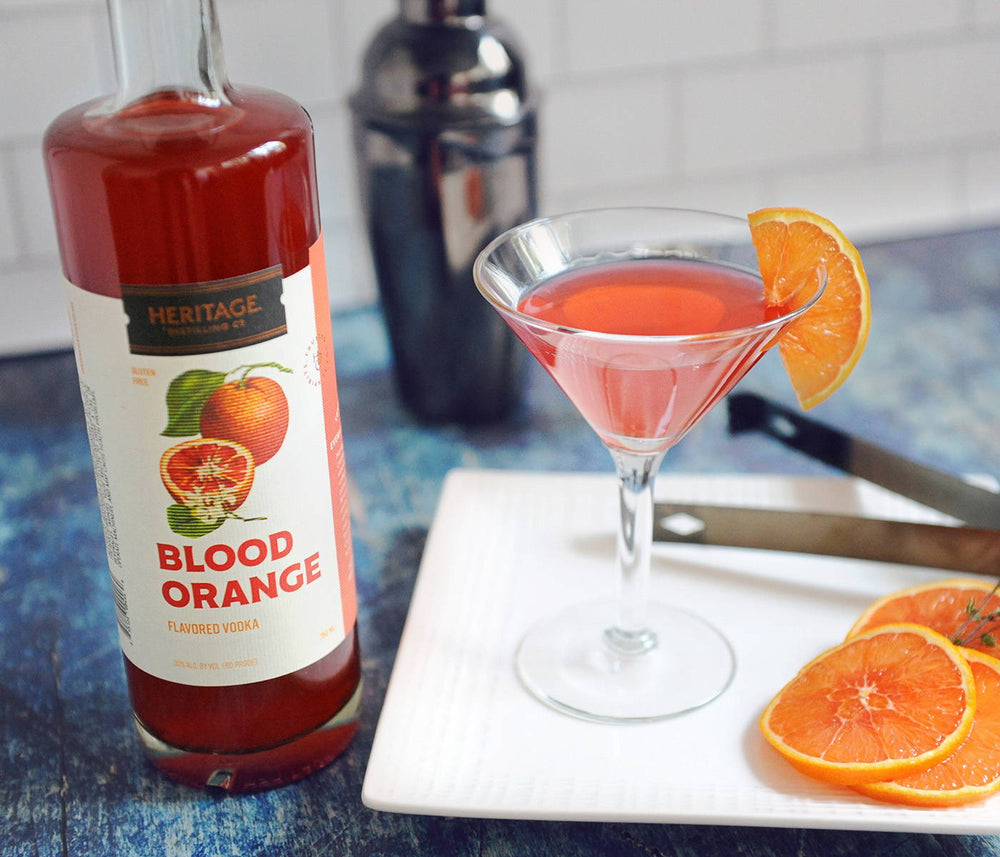 A bottle of HDC Blood Orange, a metal shaker, and a cocktail in a martini glass with blood orange garnishes.