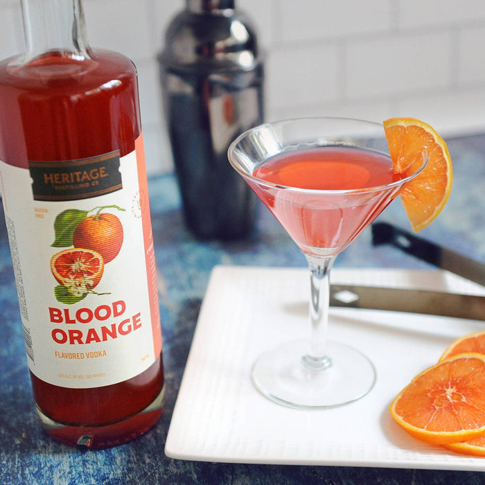 A bottle of HDC Blood Orange, a metal shaker, and a cocktail in a martini glass with blood orange garnishes.