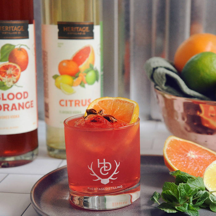 Bottles of HDC Blood Orange Vodka and HDC Citrus Vodka are shown behind this fruity cocktail. 