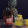 A 750ml bottle of BSB - Brown Sugar Bourbon, a whole pineapple, and a cocktail made with your choice of either BSB - Brown Sugar Bourbon or BSB 103. The garnishes are pineapple chunks.