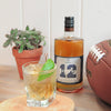 This picture shows a bottle of HDC Batch No. 12 Bourbon, a house plant, a football, and a popular cocktail with a lime.