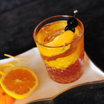 A cocktail made with HDC Dual Barrel Orange Bourbon and orange peel garnishes and cherries.