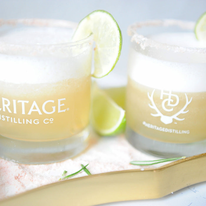 A tray holds two Heritage Distilling Co. salt rimmed glasses full of our popular spicy mango vodkaritas with lime wheel garnishes.