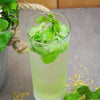 A light and refreshing light green cocktail with mint and basil leaves placed in the drink.