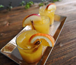 A copper tray of three spiced cider punches with orange slices, apple slices, and cinnamon sticks are on display. This cocktail is made possible by BSB - Brown Sugar Bourbon and can be served cold or warm - you choose.