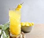 A bright yellow HDC Commander's Silver Rum and HDC Elk Rider Gin based cocktail poured into a tiki glass of ice, and garnished with pineapple chunk skewers.