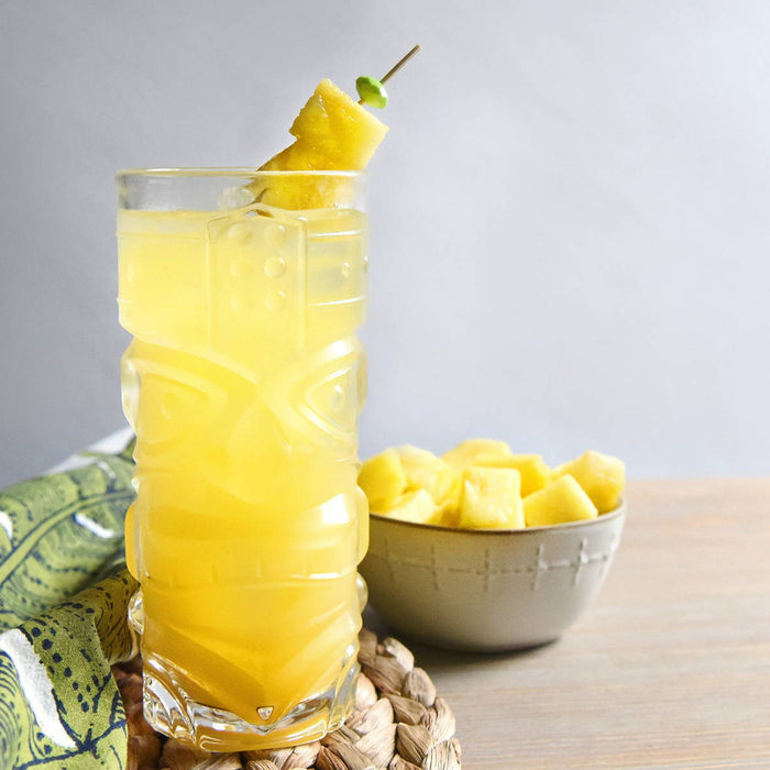 A bright yellow HDC Commander's Silver Rum and HDC Elk Rider Gin based cocktail poured into a tiki glass of ice, and garnished with pineapple chunk skewers.