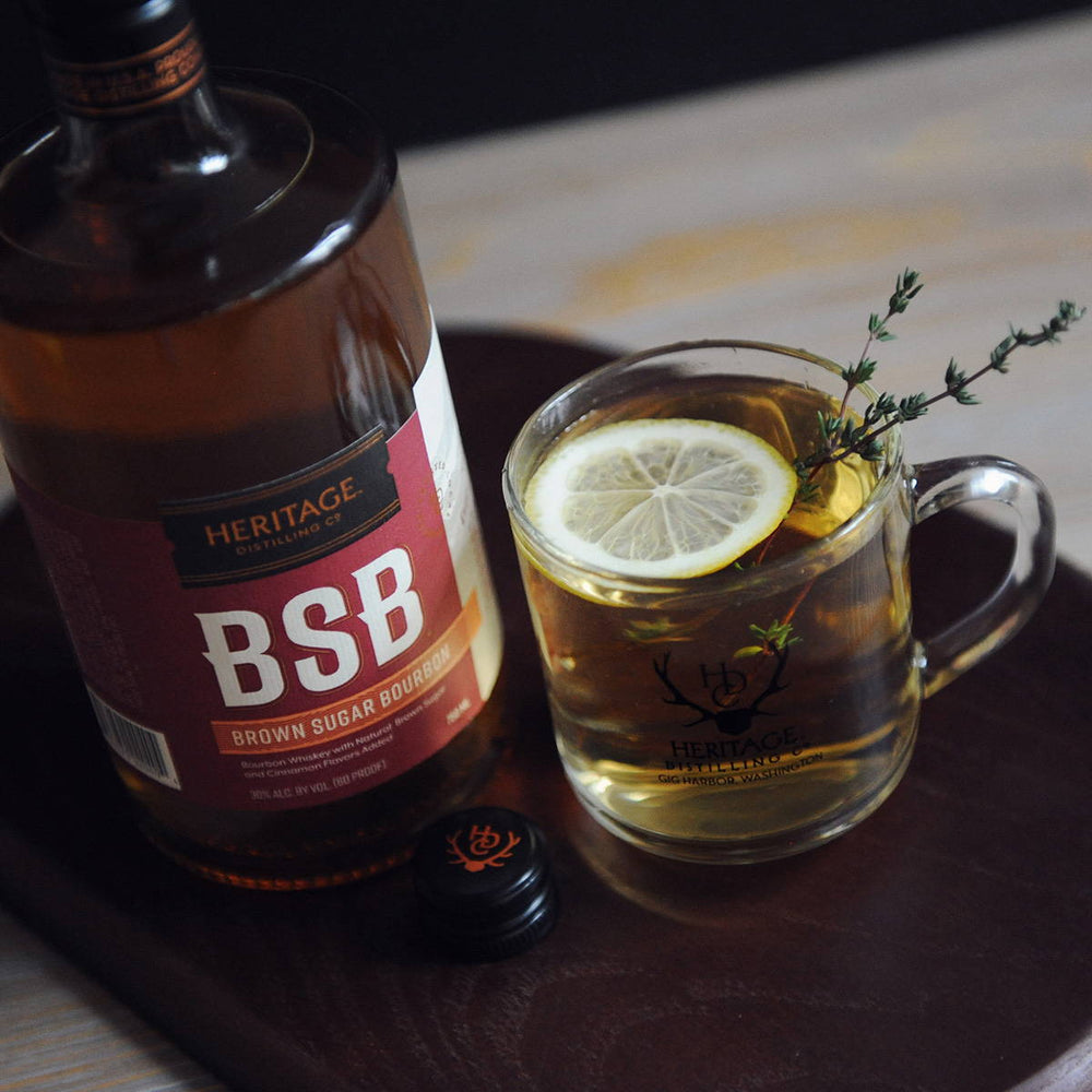 A bottle of BSB and a mug full of the BSB Brown Sugar Bourbon Toddy with a lemon slice and star anise.