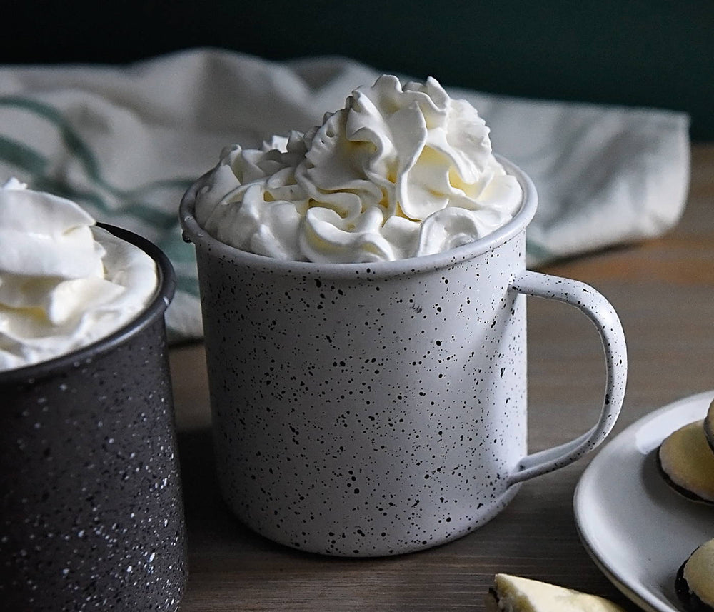 Two speckled mugs full of this hot cocktail using BSB - Brown Sugar Bourbon and is topped with whipped cream.
