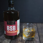 A bottle of BSB - Brown Sugar Bourbon and some BSB - Brown Sugar Bourbon poured over a single giant ice cube.