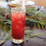 A tall glass of a HDC Elk Rider Vodka-based cocktail served with fresh rosemary sprig garnishes.