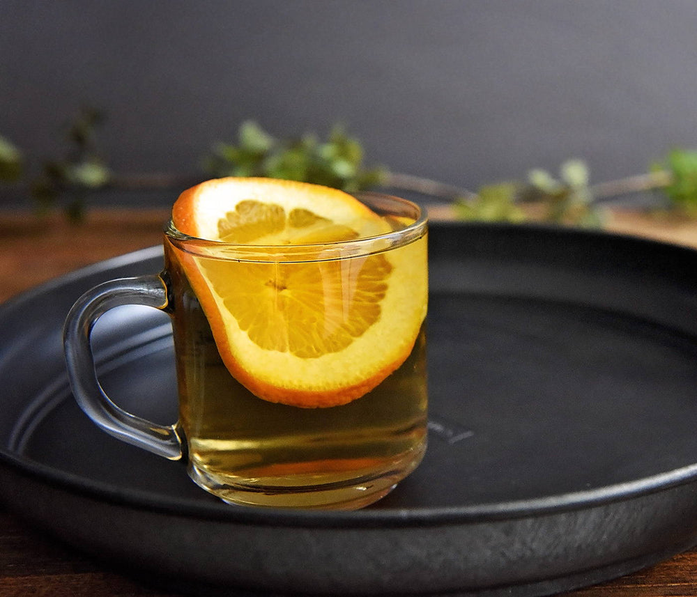 This warm mug contains a hot drink featuring BSB - Brown Sugar Bourbon and Early Grey tea. The garnishes are an orange slice and grated nutmeg.