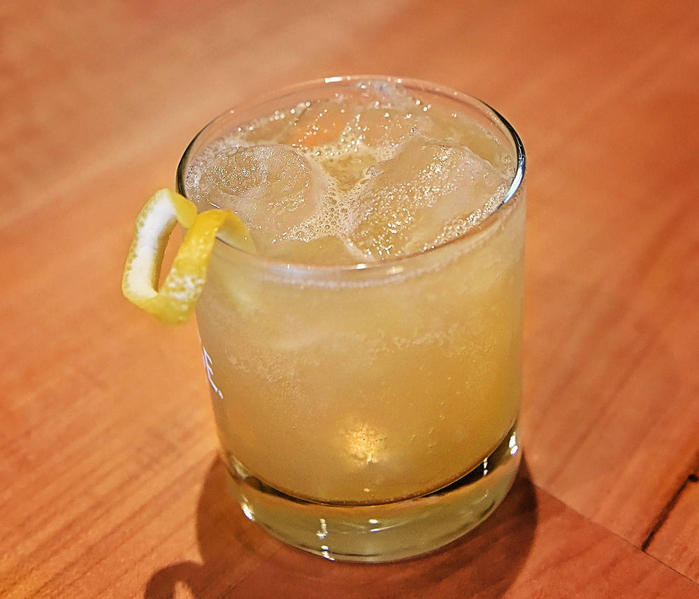 A gin based cocktail poured over ice and garnished with a lemon twist.
