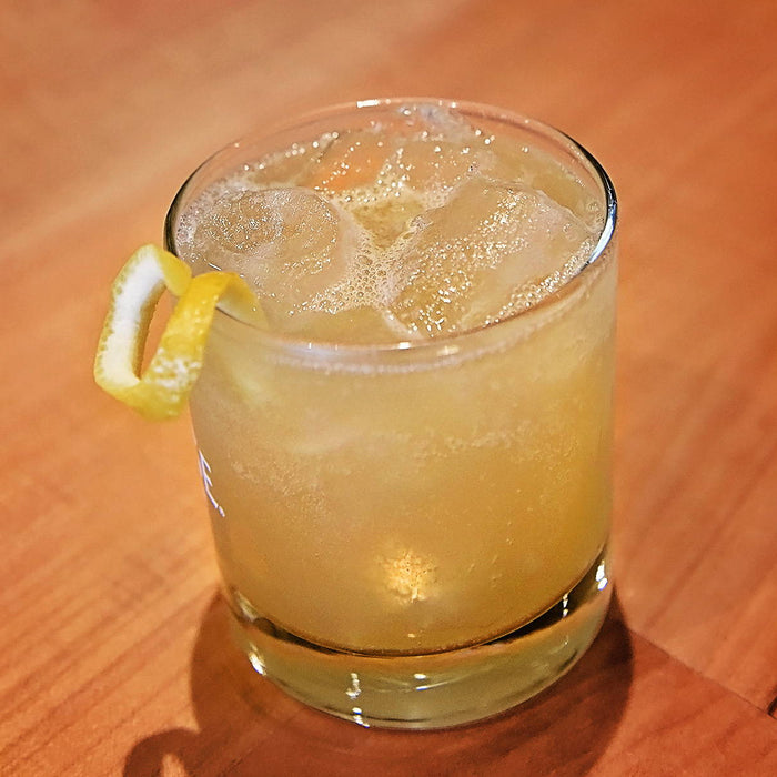 A gin based cocktail poured over ice and garnished with a lemon twist.