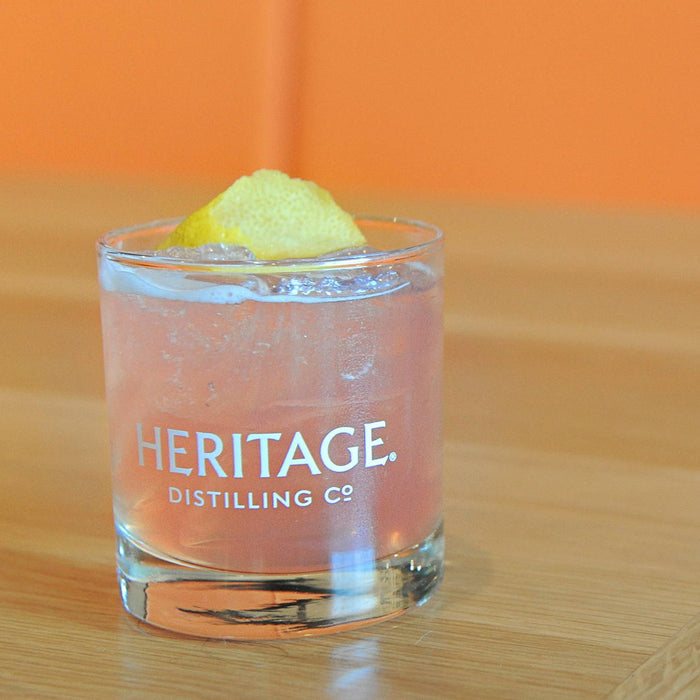 A light pink cocktail featuring HDC Peach Vodka in a Heritage Distilling Co. tumbler with a lemon wedge garnish.