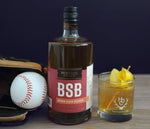 A bottle of BSB - Brown Sugar Bourbon (next to a baseball glove and baseball) and the Knuckleball cocktail with a lemon peel garnish.