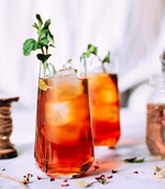 Two tall glasses of raspberry palmer cocktails with ice and sprigs of mint to garnish them.