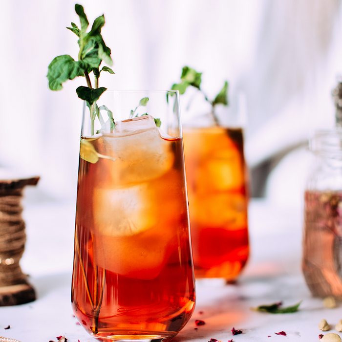 Two tall glasses of raspberry palmer cocktails with ice and sprigs of mint to garnish them.