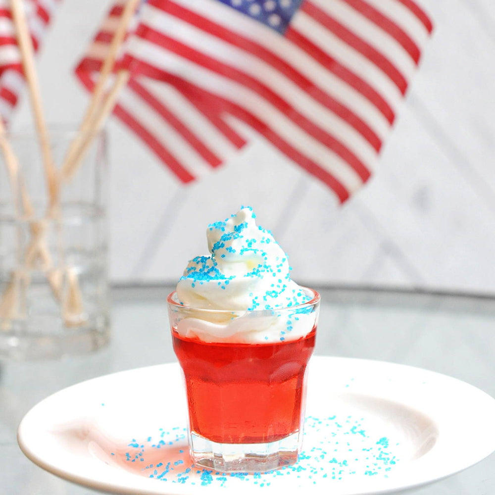 A red jello shot is pictured with American flags in the background. These Jell-o shots can be made with any of our HDC flavored vodka selections.
