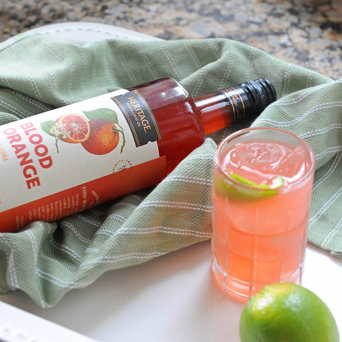 A bottle of HDC Blood Orange Vodka & a pink HDC Blood Orange cocktail with a lime wedge.