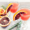 Two cocktail glasses filled with a pink gin cocktail and blood orange wedges to garnish them.