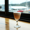 Pinkish orange tinted cocktail with a lemon garnish photographed on a window ledge