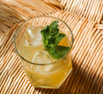 Geometric shaped rocks glass with bright yellow bourbon cocktail served over ice and a fresh mint garnish