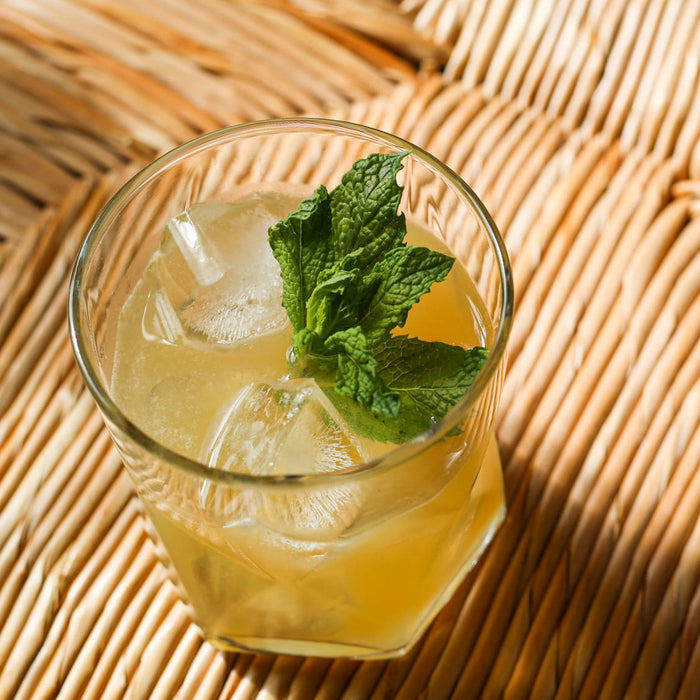 Geometric shaped rocks glass with bright yellow bourbon cocktail served over ice and a fresh mint garnish