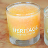 A Heritage Distilling Co. rocks glass is filled with an orange-ish yellow colored frozen slush drink.