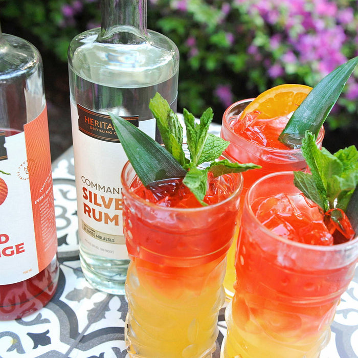 A bottle of HDC Blood Orange Vodka and a bottle of HDC Commander's Silver Rum are pictured here. There are also two full cocktails using a mix of these two spirits as well as mixers.