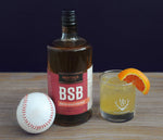 A bottle of BSB - Brown Sugar Bourbon and a baseball. The "Fastball" Cocktail in a tumbler full of ice with an orange slice garnish.