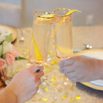 Two people cheers their gold-rimmed champagne flutes are filled with a HDC Vanilla Vodka-based cocktail that is garnished with a long lemon peel.