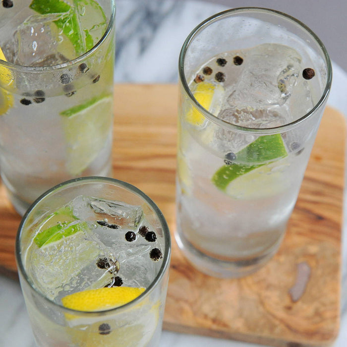 Three highball glasses of a cocktail made with HDC Bestemors Aquavit and garnished with lemon, lime, and peppercorns.