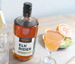 A 750ml bottle of HDC Elk Rider Rye Whiskey and a cocktail in a cocktail goblet.