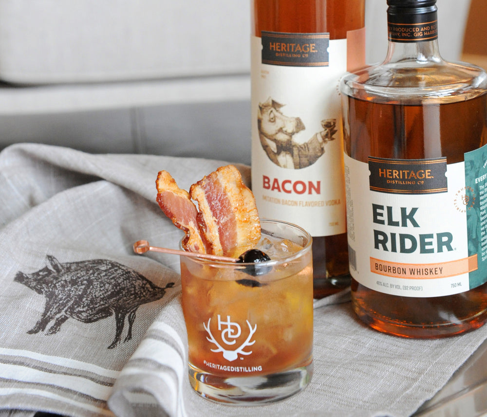 
                  
                    A 750ml bottle of HDC Bacon Vodka and a 750ml bottle of HDC Elk Rider Bourbon Whiskey next to a popular old fashioned cocktail using those two spirits.
                  
                